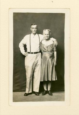 STANDING ELDERLY COUPLE, HAND AROUND SHOULDERS, MAN IN SUSPENDERS (FOREST GOFF & WIFE ADA GOFF)