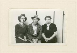 SEATED MAN IN HAT FLANKED BY TWO SEATED WOMEN, STRIPED BACKGROUND