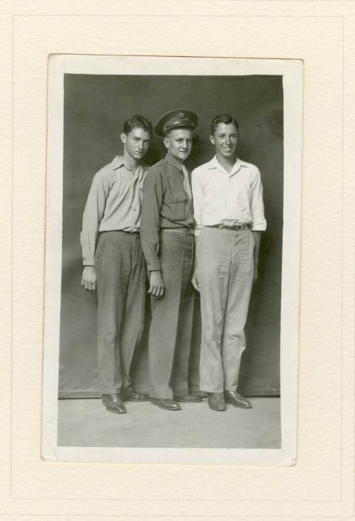 THREE STANDING MEN, ONE WITH MILITARY CAP