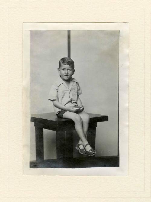 SEATED BOY ON TABLE, STRIPED BACKGROUND
