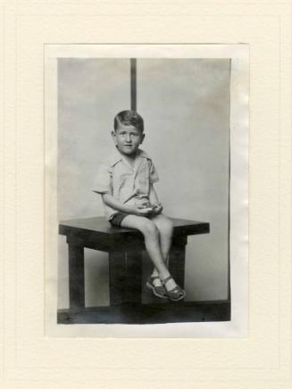 SEATED BOY ON TABLE, STRIPED BACKGROUND
